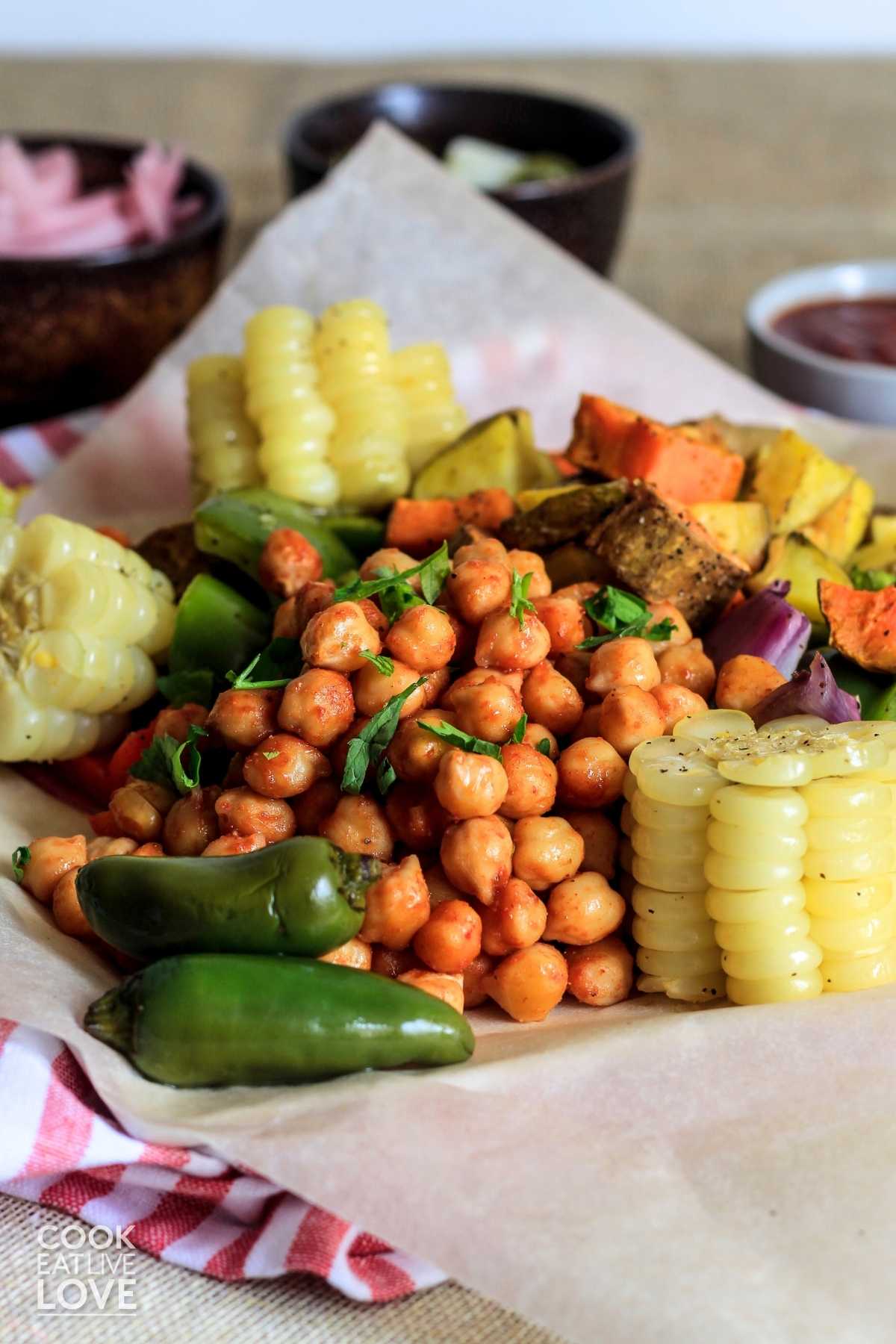 BBQ chickpeas and veggies on baking paper with sauce and jalapenos.