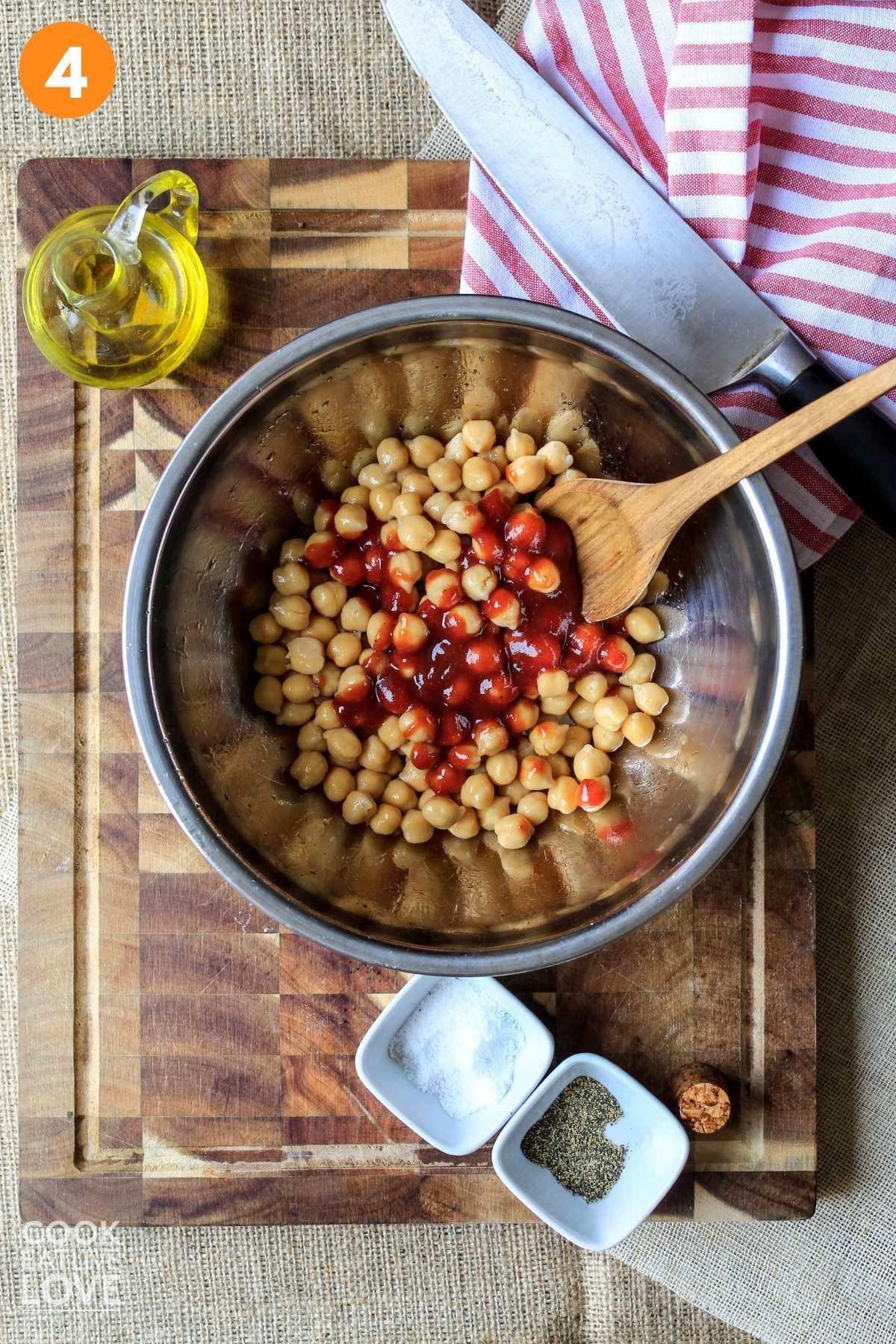 Chickpeas in a metal bowl with bbq sauce on top and a spoon in the bowl.