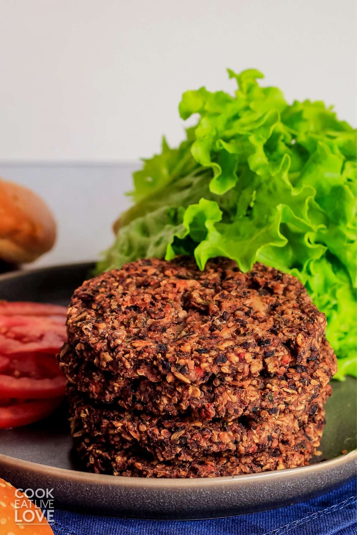 Stack of black bean quinoa burgers on a plate with leaf lettuce and tomato slices.