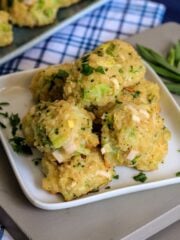 Cheese and broccoli bites are stacked up on a white plate on the table.