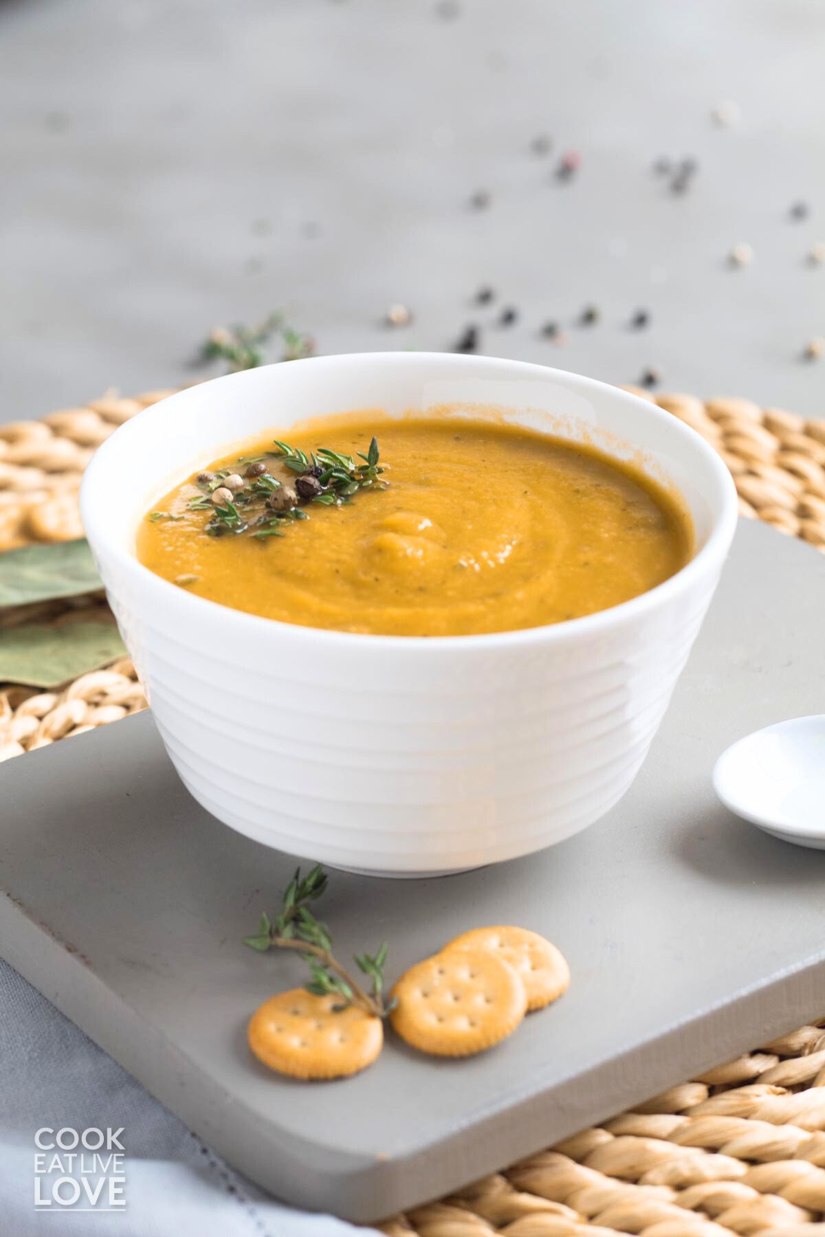 Bowl of cauliflower carrot soup on the table with thyme and peppercorns for garnish.