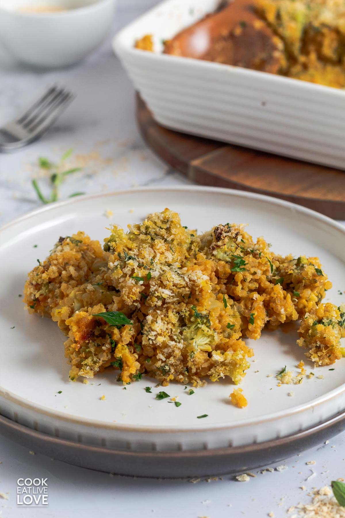 Cheesy quinoa casserole served up on a white plate with the casserole dish in the background.