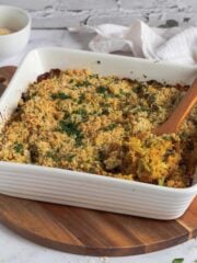 Cheesy broccoli in a white baking dish with a spoon lifting some out.