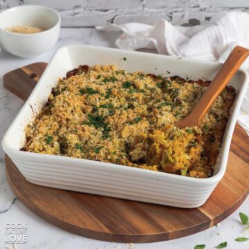 Cheesy broccoli in a white baking dish with a spoon lifting some out.