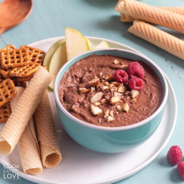 A bowl of chocolate hummus with fruit and cookies on a table.