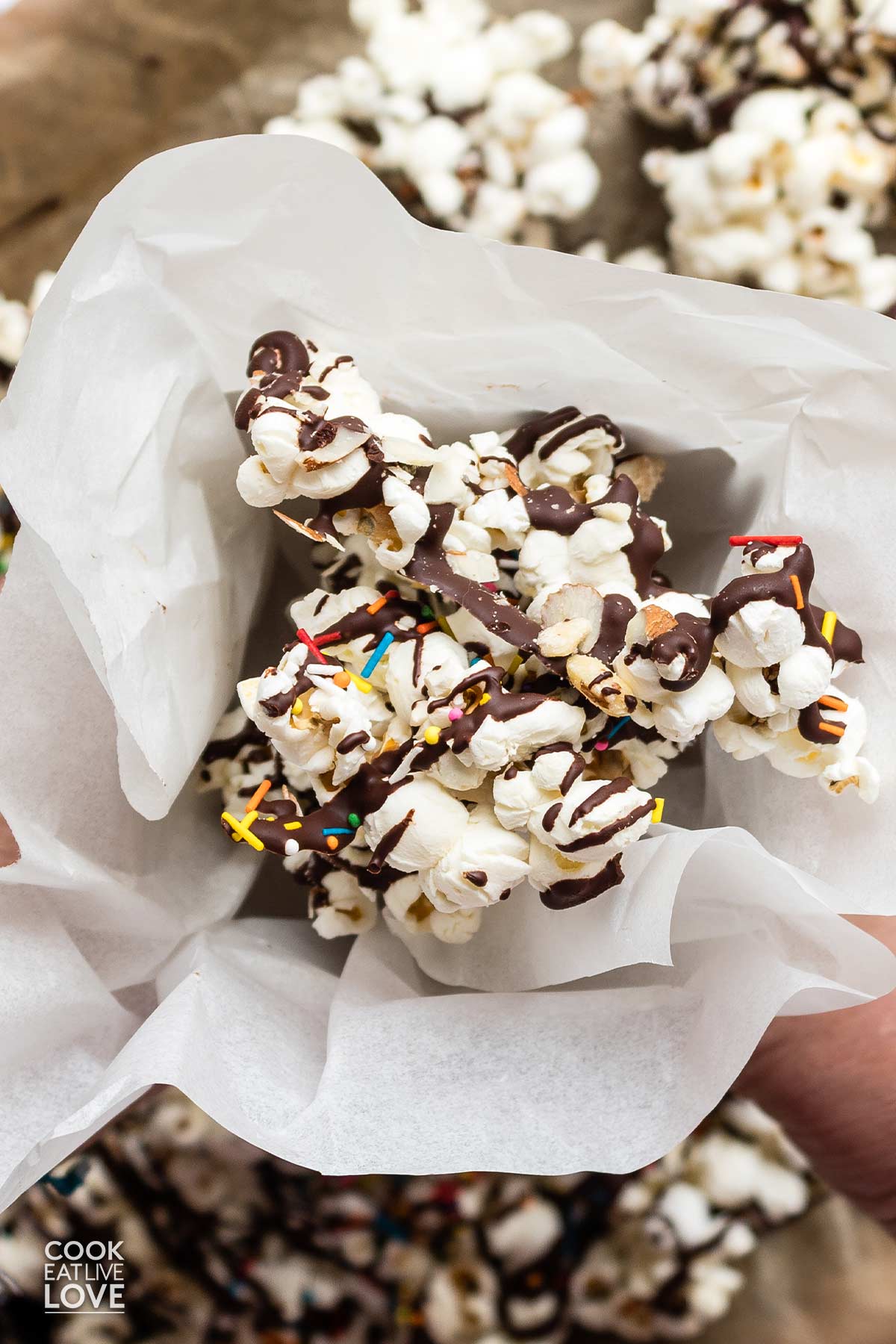 Hands holding a bucket of chocolate drizzled popcorn over the tray of prepped popcorn.