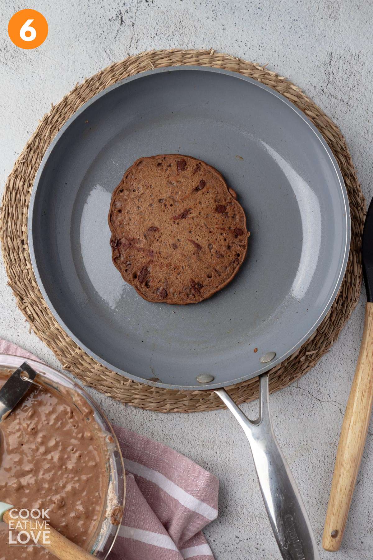 Chocolate pancake flipped over in a skillet to cook the other side.