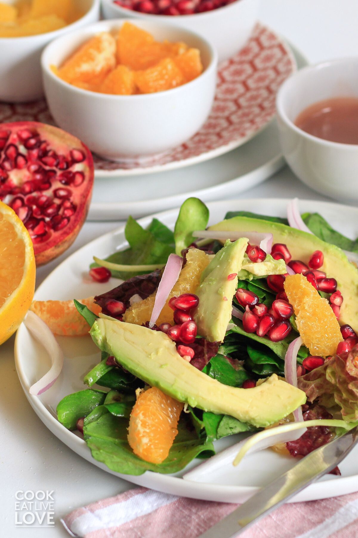 A citrus avocado salad on a plate with bowls of ingredients and dressing in the background.