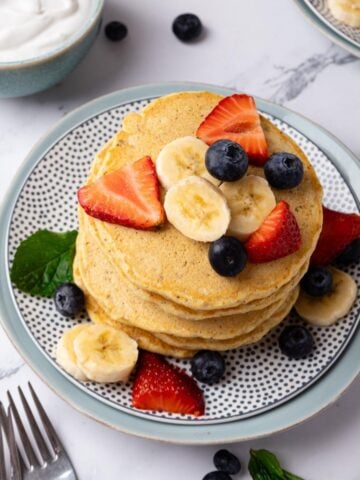 Overhead of plate of savory corn pancakes with egg on top. Fork to the side and the yolk is broken and oozing out over the pancakes.