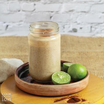 Chipotle yogurt sauce in a jar on a plate with limes and a spoonful of chipotle powder.