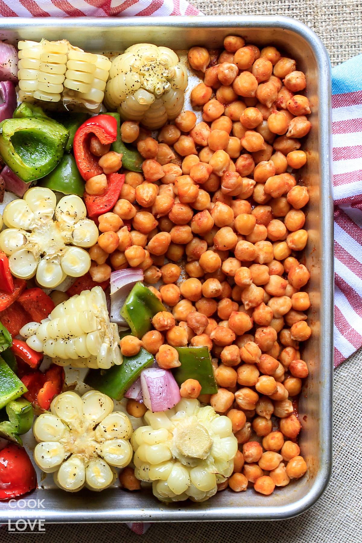 Chickpeas on a baking tray with corn, bell pepper, and onion.