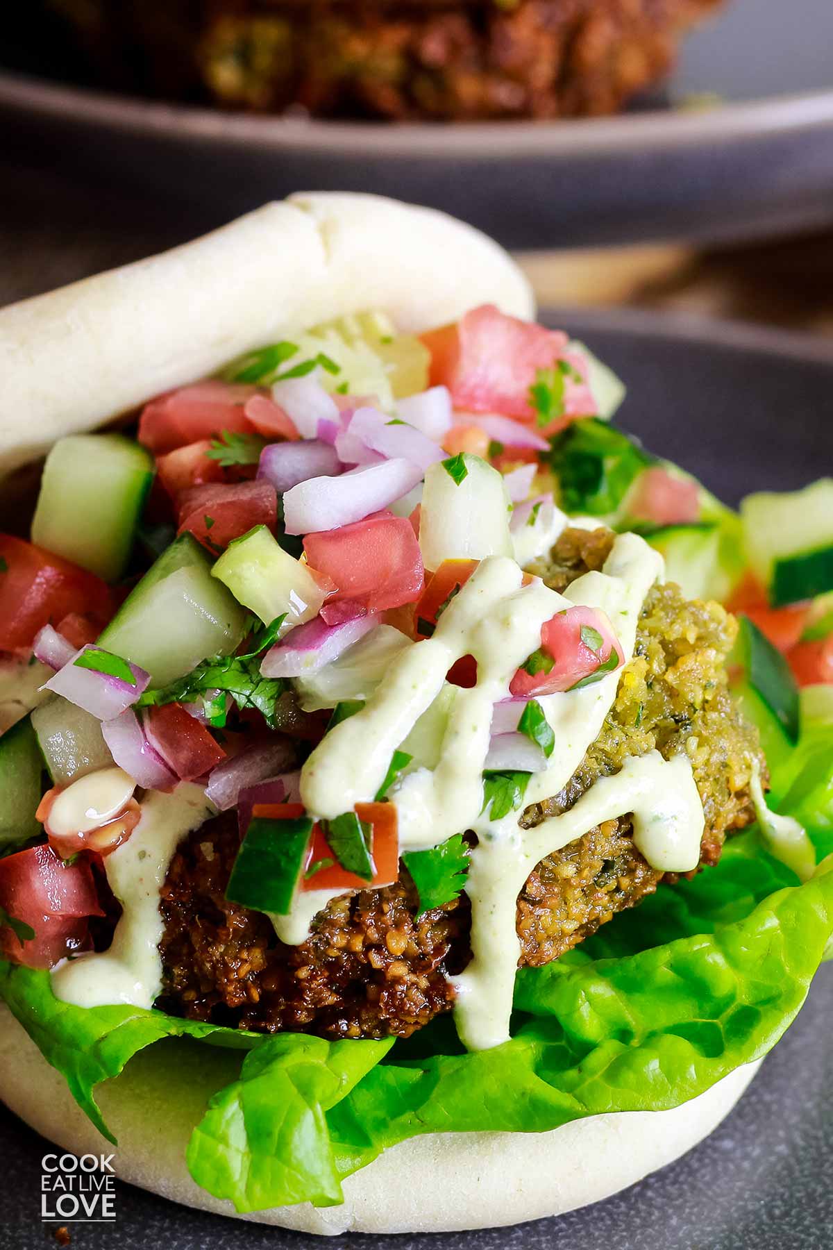 A falafel burger with lemon tahini sauce and cucumber topping on a plate.
