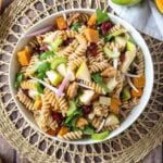 Fall pasta salad in white bowl on a wicker placemat on a wooden table.