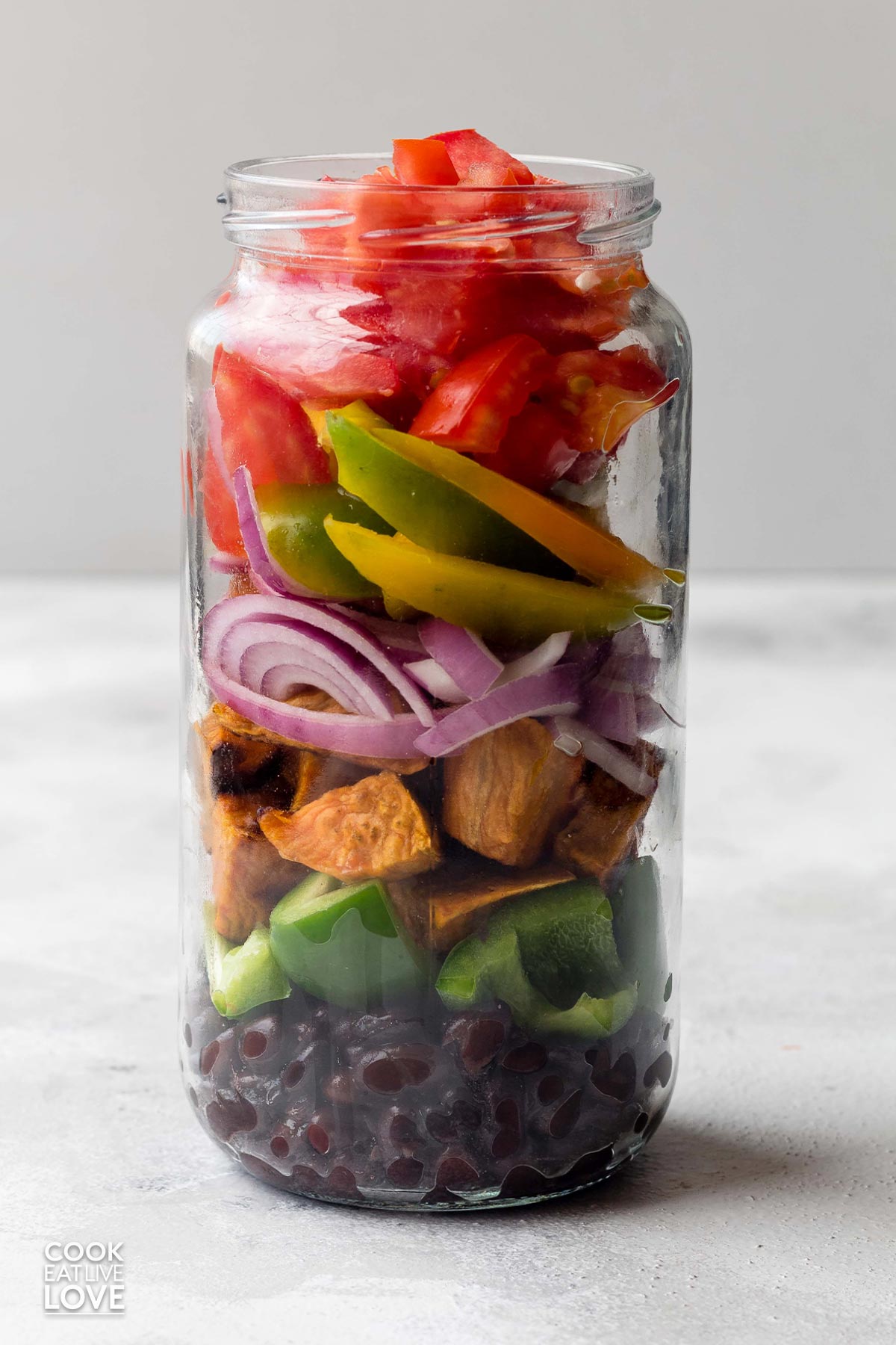 A jar of vegetarian salad on the counter with each ingredient making up a layer.