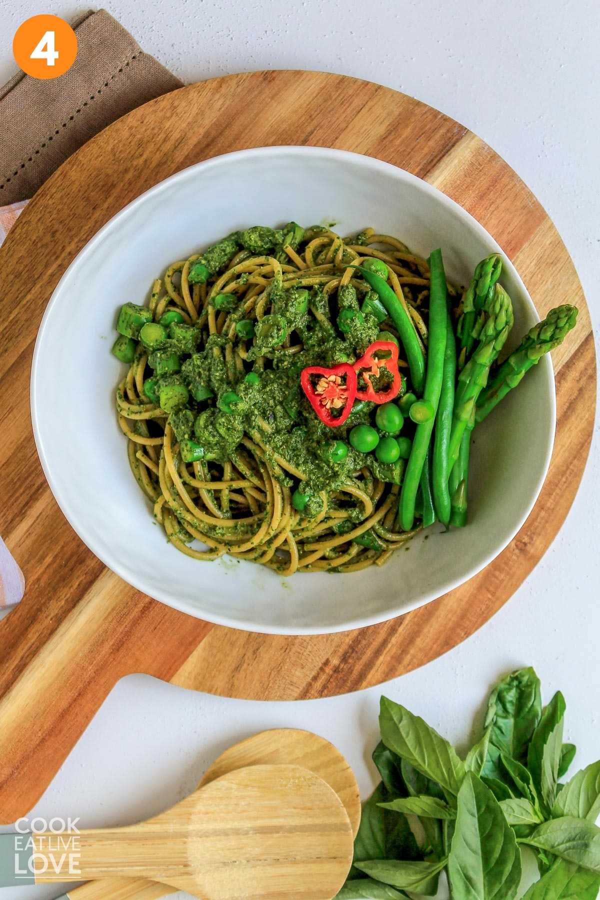 Green spaghetti served up in a bowl topped with veggies.
