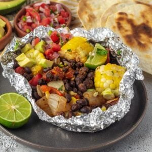 A grilled veggie foil packet served up for a hobo dinner with black beans, veggies, and corn.