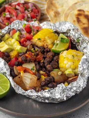 A grilled veggie foil packet served up for a hobo dinner with black beans, veggies, and corn.