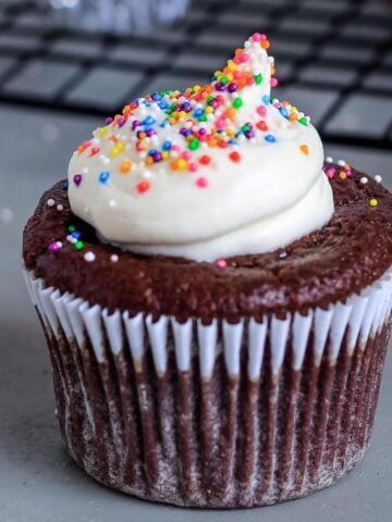 Healthy cupcakes without eggs on the counter with one in the front topped with white frosting and sprinkles.