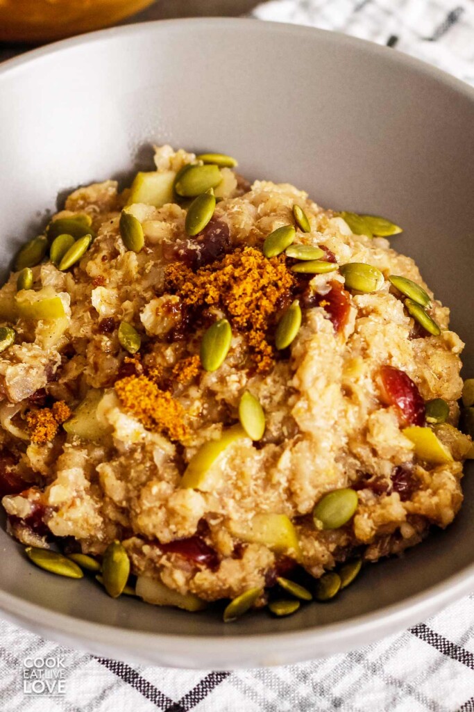 A closeup overhead view of a gray bowl of quinoa flakes porridge topped with panela and pumpkin seeds.