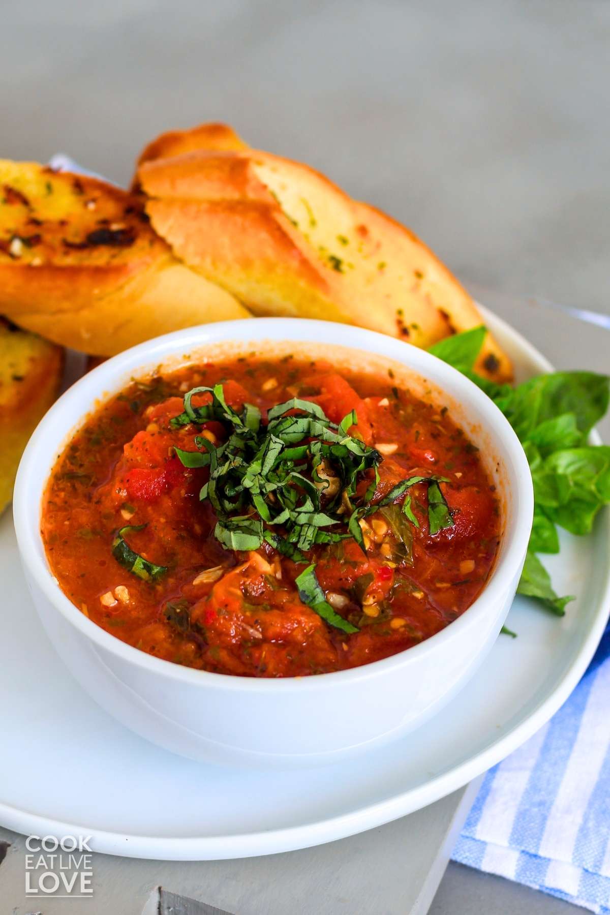 Hearty tomato sauce in a bowl on a plate with garlic bread and garnished with julienned fresh basil.