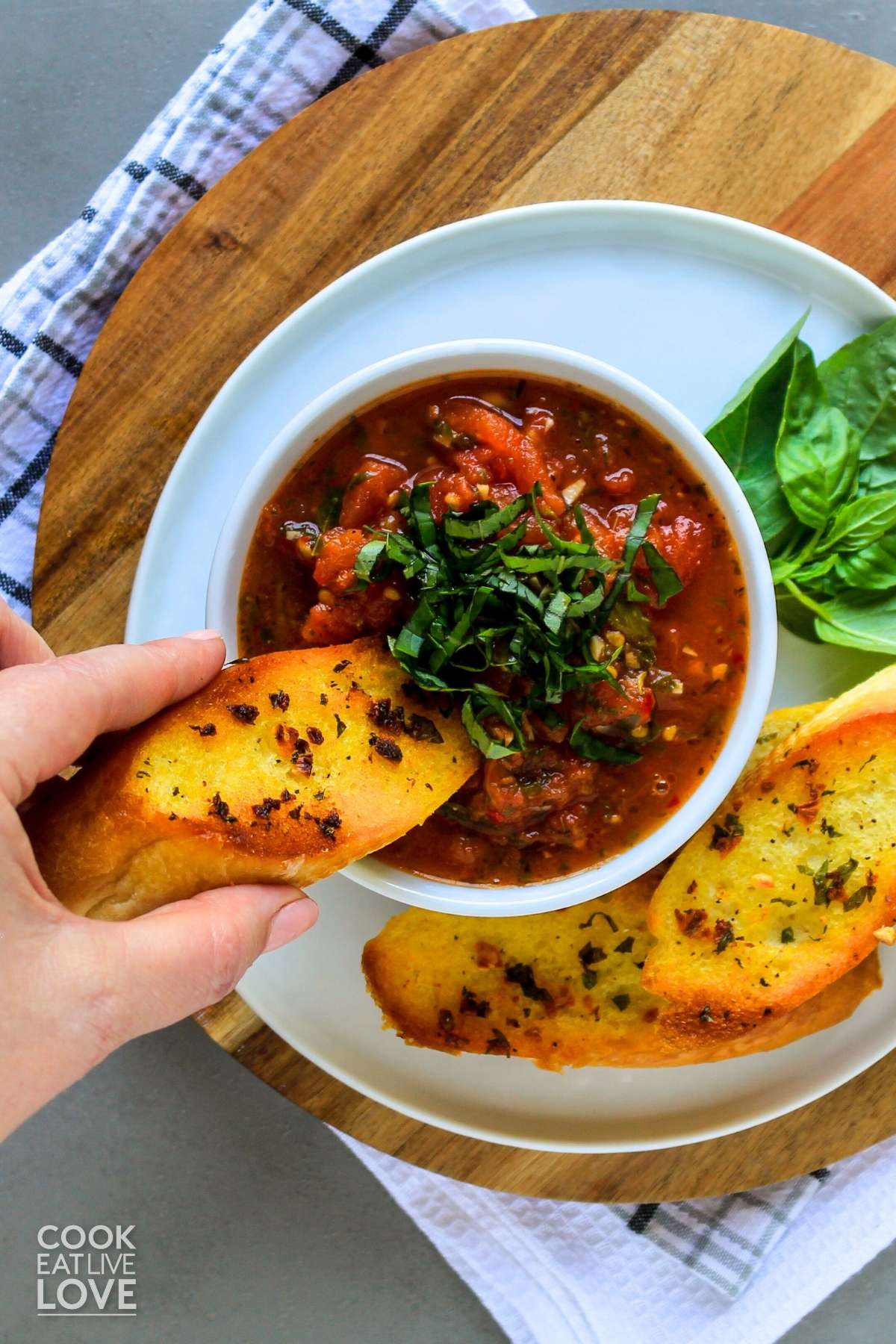 Hearty tomato sauce in bowl and a hand reaching in to dip a piece of garlic bread.