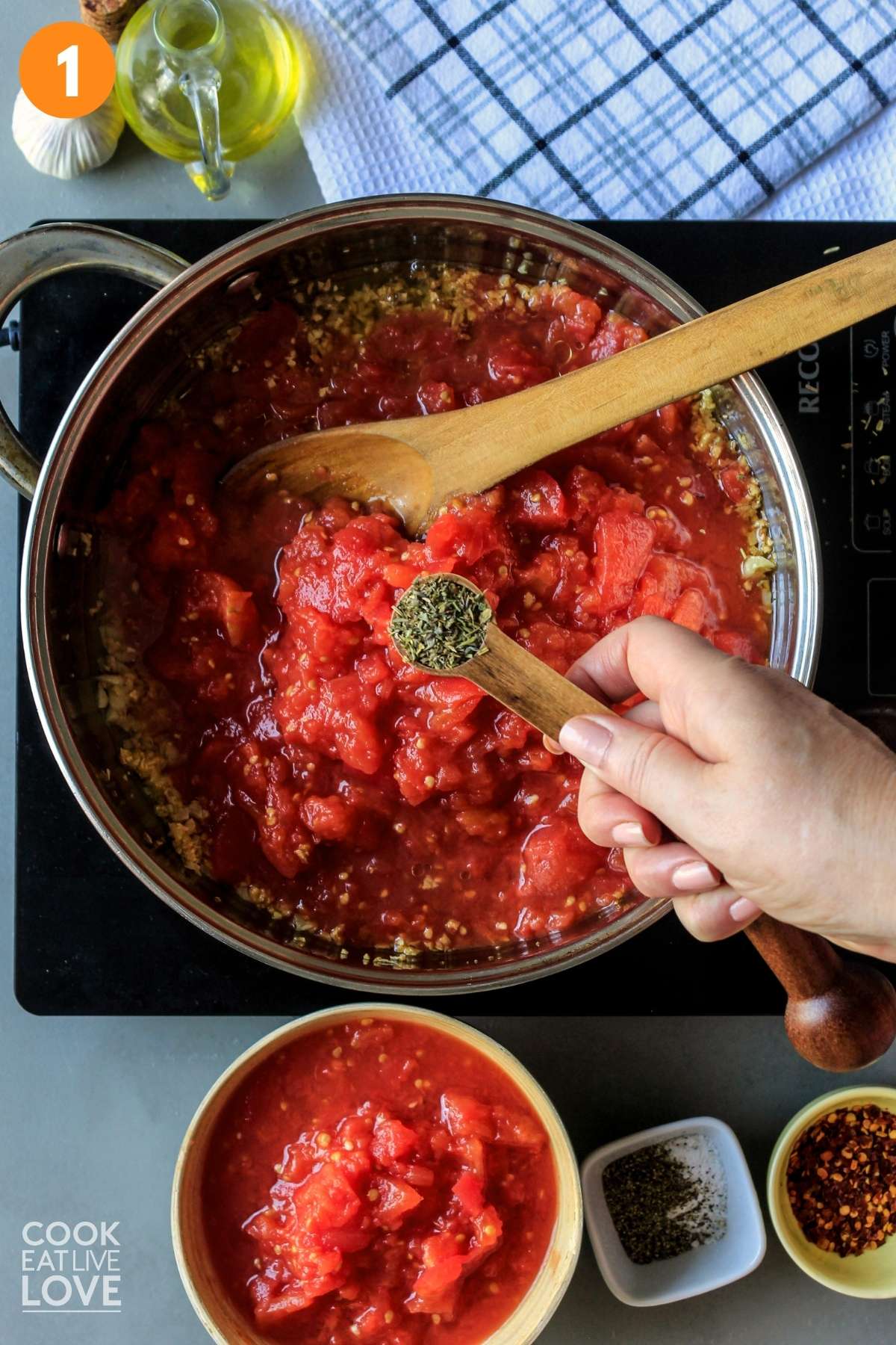 Tomatoes added to the skillet and a hand holding a measuring spoon of Italian seasoning over the pan.