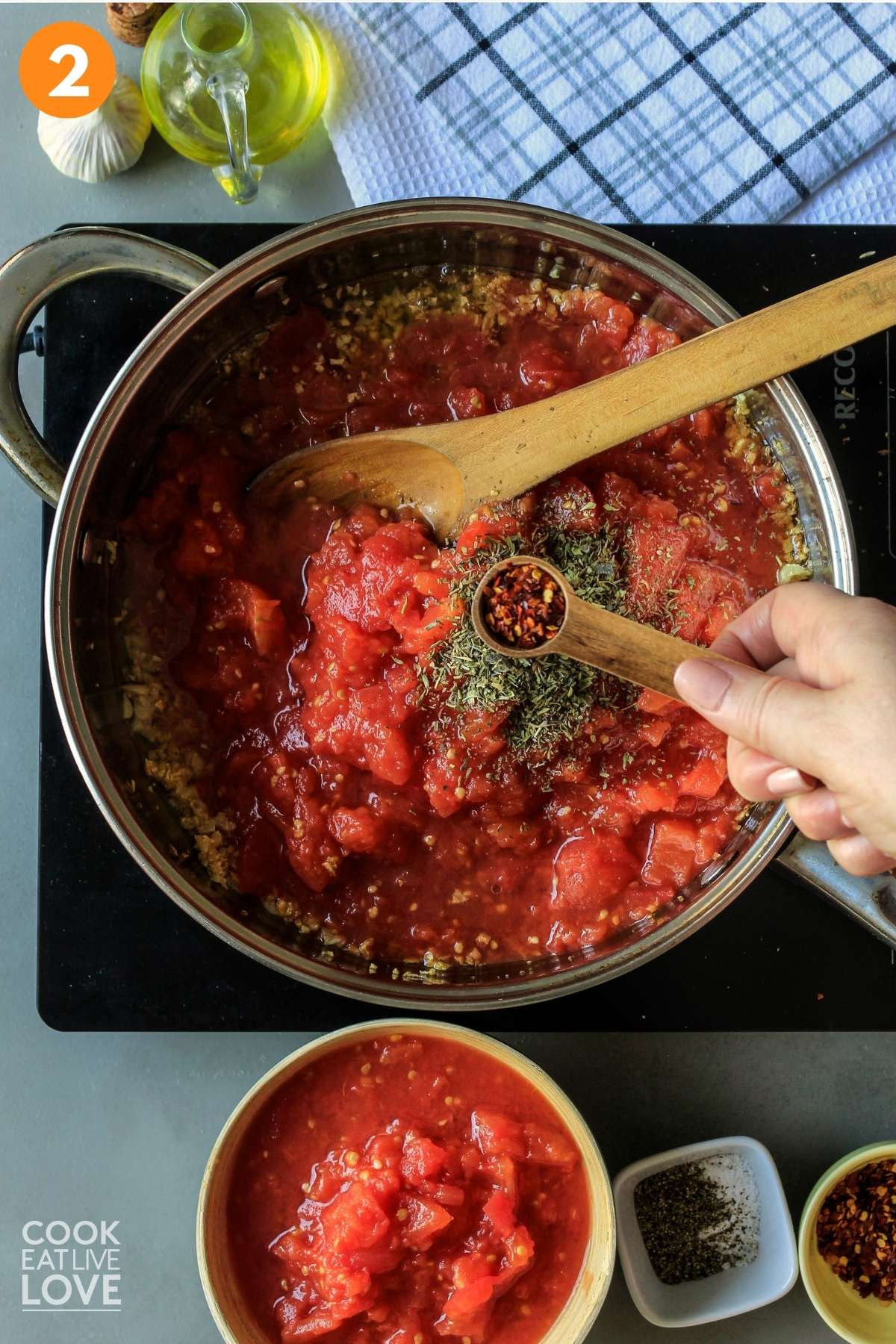 A measuring spoon of red pepper flakes over the pan of hearty tomato sauce.