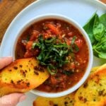 A bowl of hearty marinara sauce with a piece of bread dipping into the bowl.