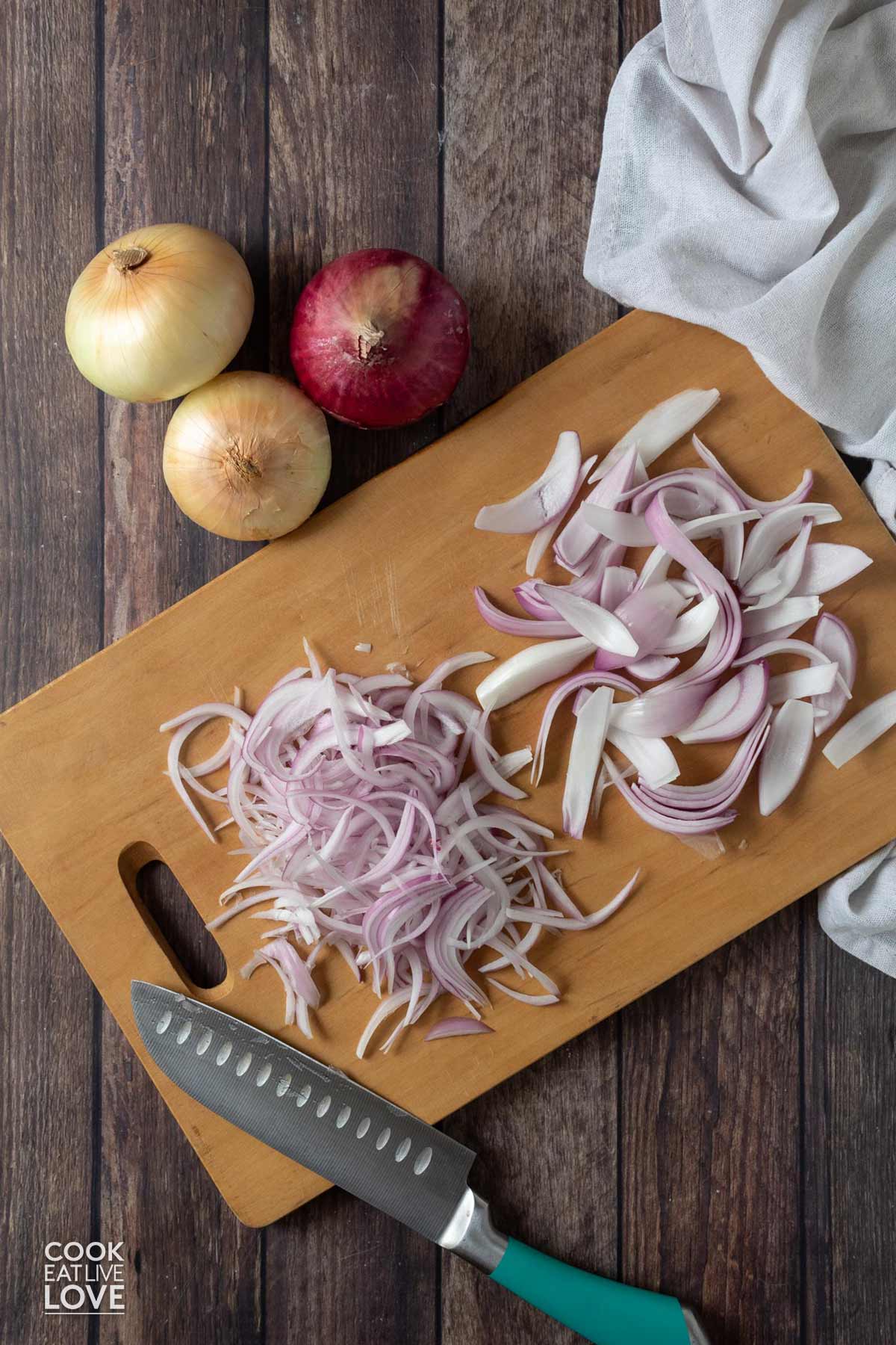 Red onions cut into thin and thick strips on a cutting board.