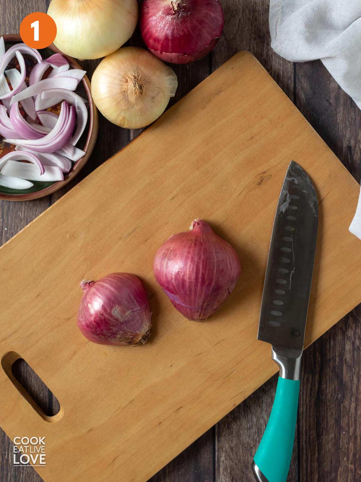 Onion cut in half with flat side down and a knife next to it on the cutting board.