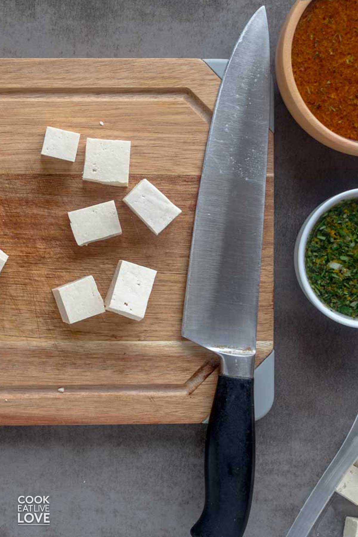 Cubes of tofu cut on a cutting board with a knife.