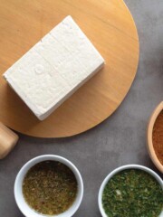 A block of tofu on a cutting board with bowls of marinades.