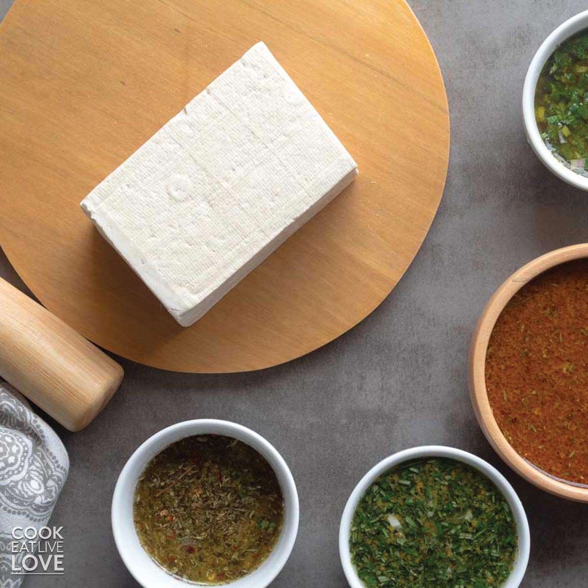 A block of tofu on a cutting board with bowls of marinades.