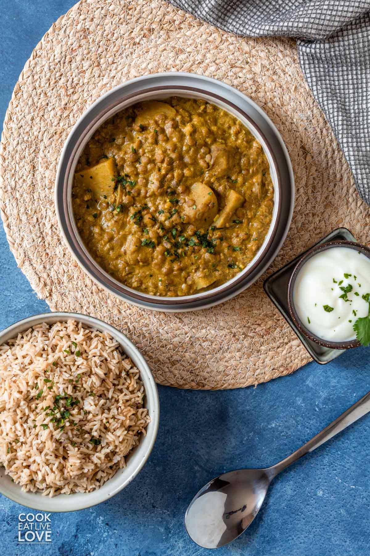 Lentil curry in a bowl on the table with a bowl of yogurt and a bowl of rice next to it.