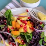 Mango salad on white plate with jar of avocado dressing.