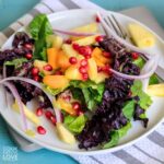 A mango avocado salad on a white plate with a gray and white napkin underneath it.