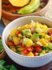 A bowl of 5 ingredient mango salsa on the table with fresh produce around it.