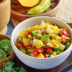 A bowl of 5 ingredient mango salsa on the table with fresh produce around it.