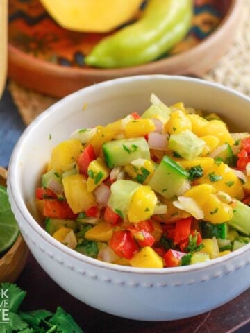 A bowl of 5 ingredient mango salsa on the table with fresh produce around it.