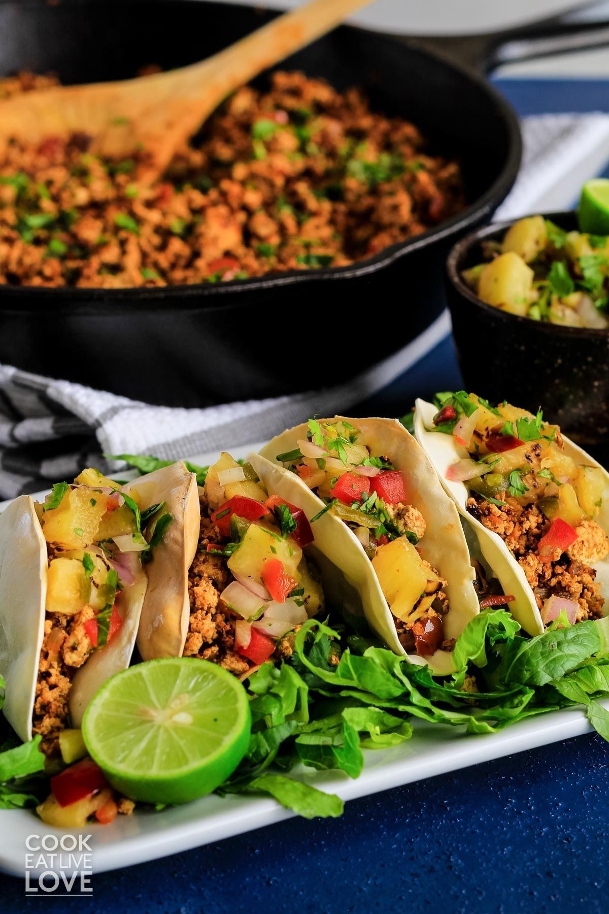 Rectangle white plate filled with mini taco bites garnished with lime and lettuce, salsa and pan of tofu filling in background.