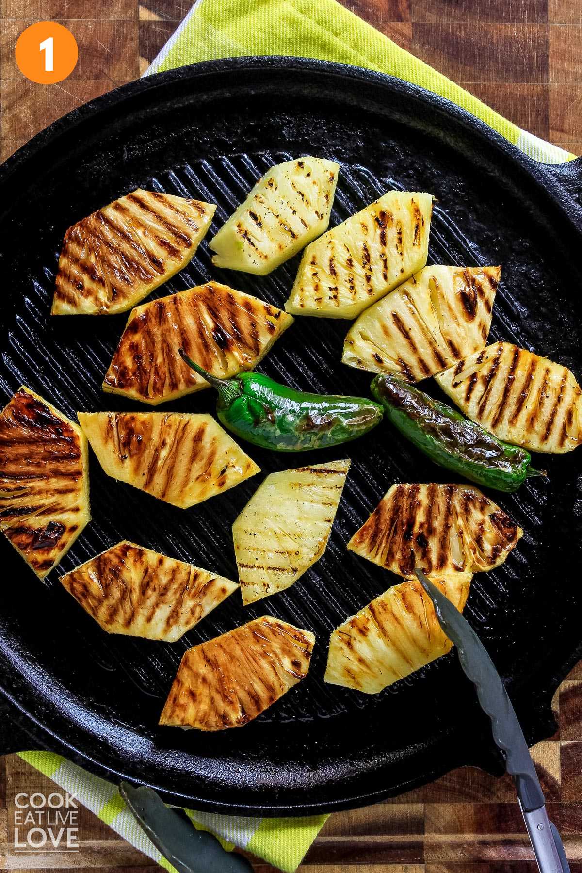 Slices of pineapple on a grill pan with jalapeno in the middle.