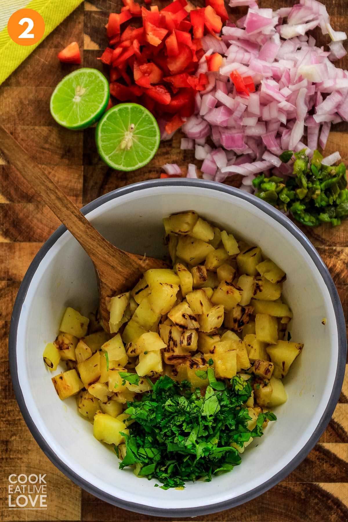 Pineapple and cilantro in white bowl with onions, red pepper and limes to juice on the side.