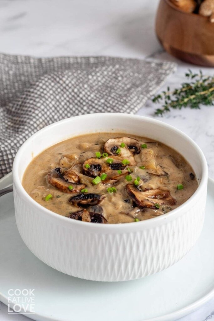 Mushroom sauce in a bowl on the table with a sprig of thyme and bowl of mushrooms in the back.
