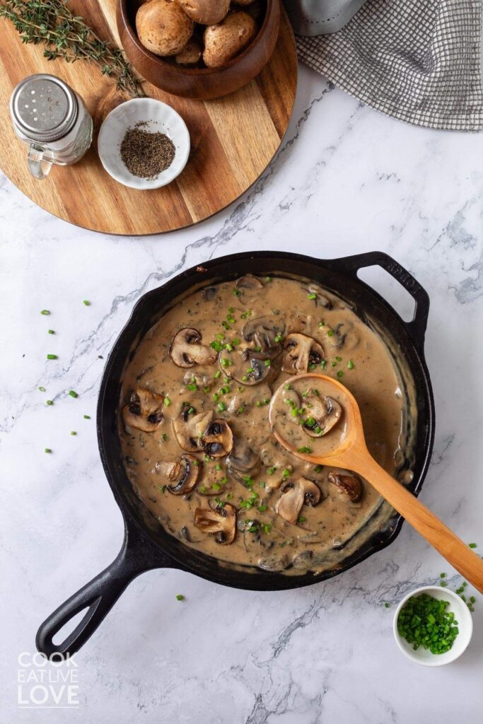 Vegan mushroom sauce in skillet with wooden spoon.  To the side are whole mushrooms and parsley.