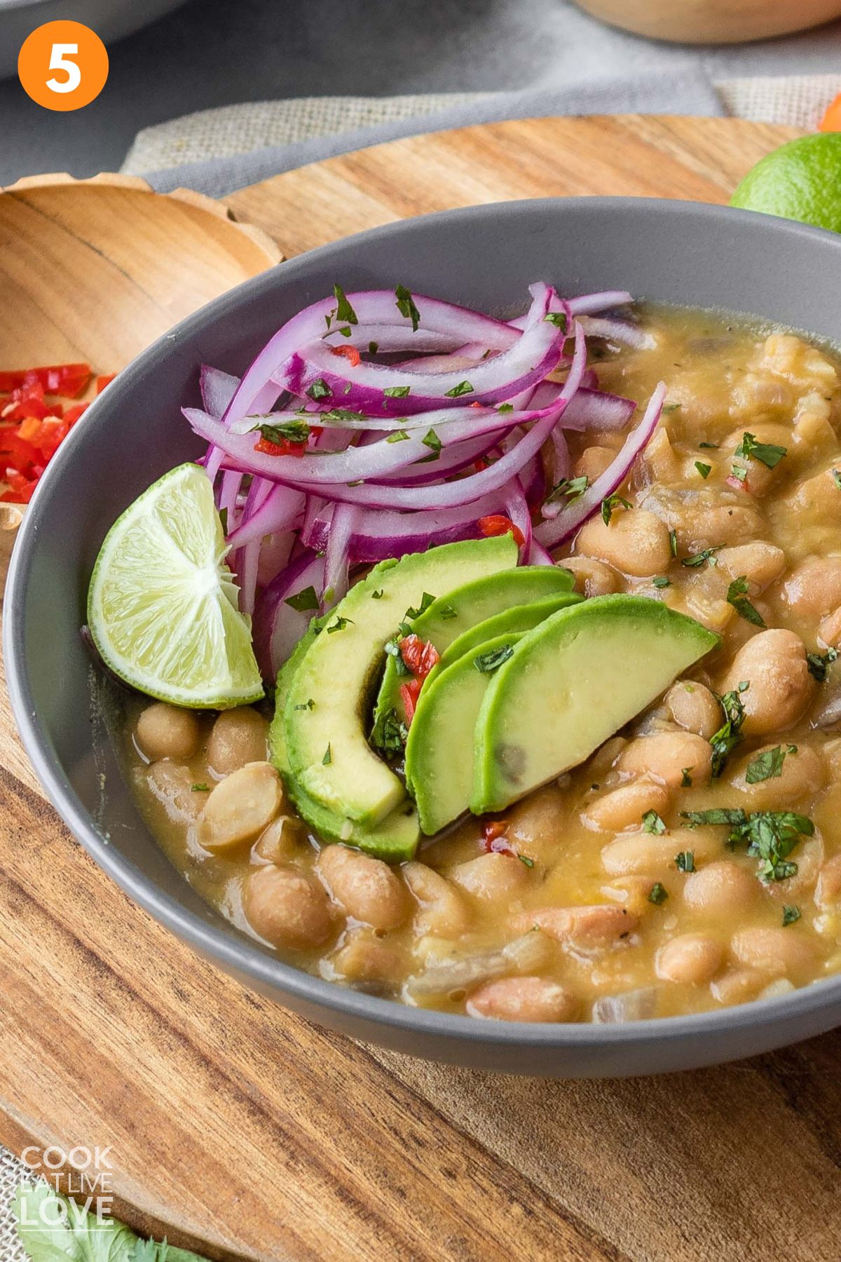 A bowl of peruano beans on the table with avocado and onion.