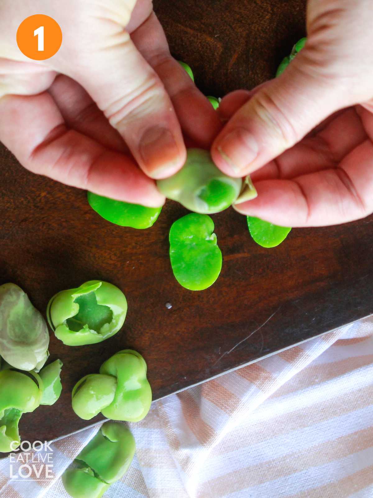 Hands peeling the fava beans for Peruvian chopped salad.