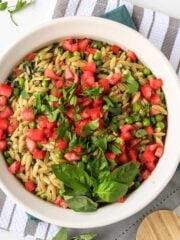 Pesto orzo in a skillet with wooden spoon and topped with tomatoes