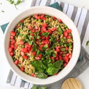 Pesto orzo in a skillet with wooden spoon and topped with tomatoes