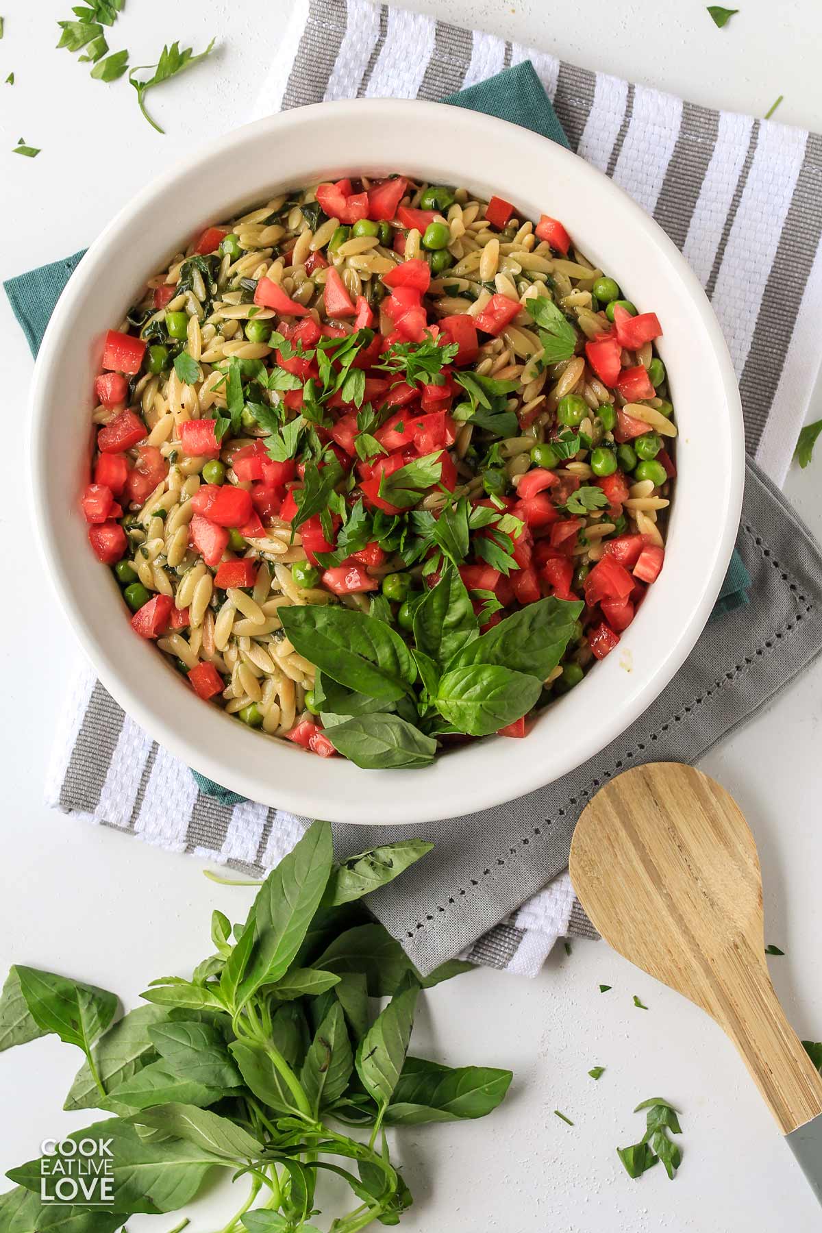 Pesto orzo side dish is served up in a large white serving bowl with tomatoes and fresh basil.