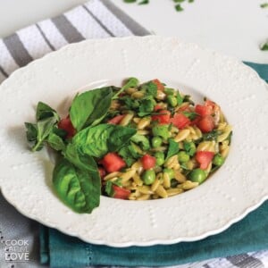 Pesto orzo in a skillet with wooden spoon and topped with tomatoes